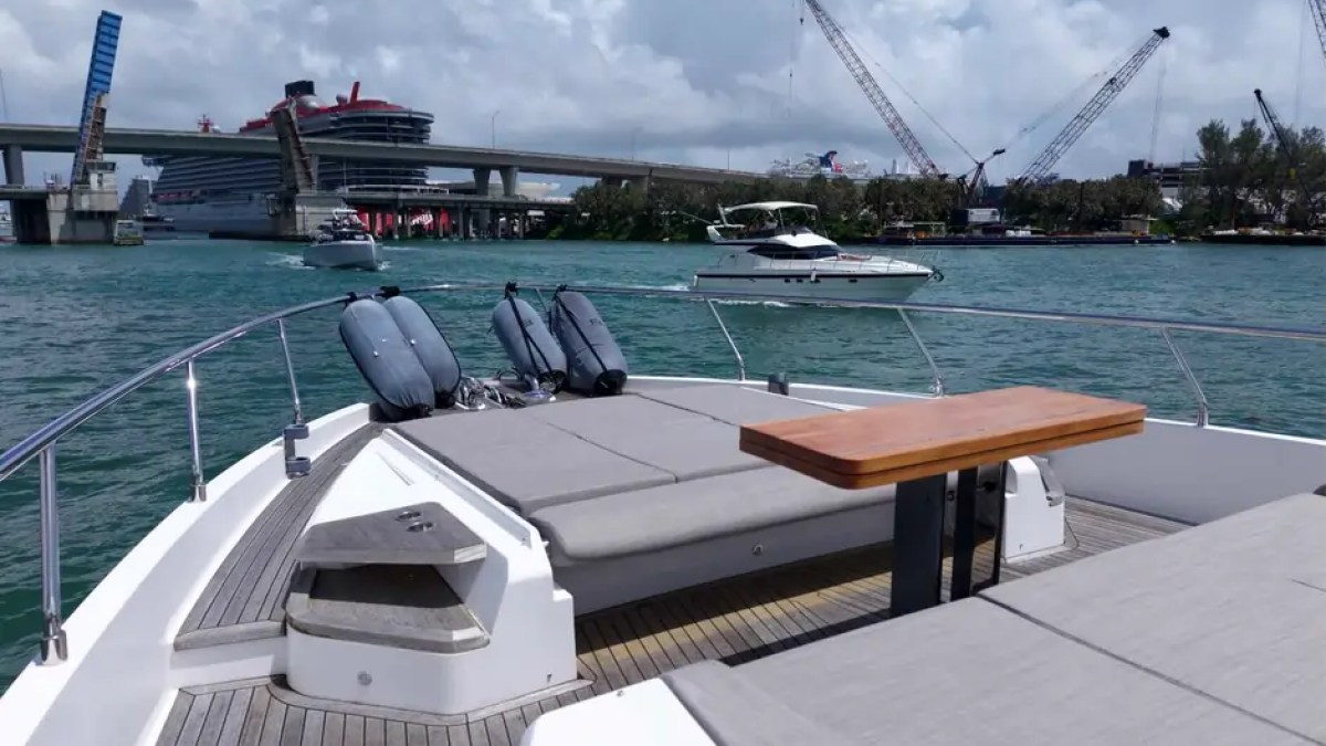 80' Ferretti Yacht Charter bow lounge with sun pads and teak table cruising Miami waters.
