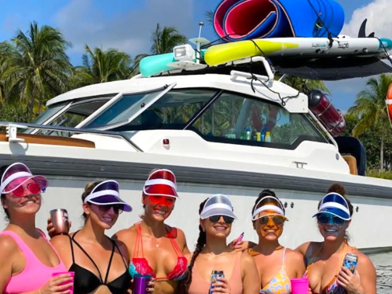 Friends enjoying a tropical sandbar party beside a 26' Axopar Boat Rental with paddleboards and water toys in Riviera Beach.