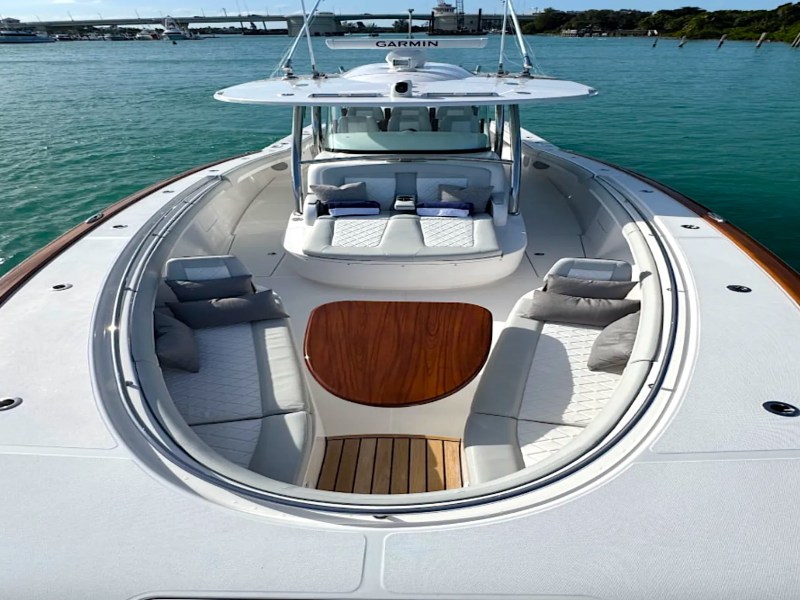 Forward lounge aboard the 43' Mag Bay Boat Rental in Riviera Beach featuring wraparound seating, teak table, sun pad, and Garmin hardtop.