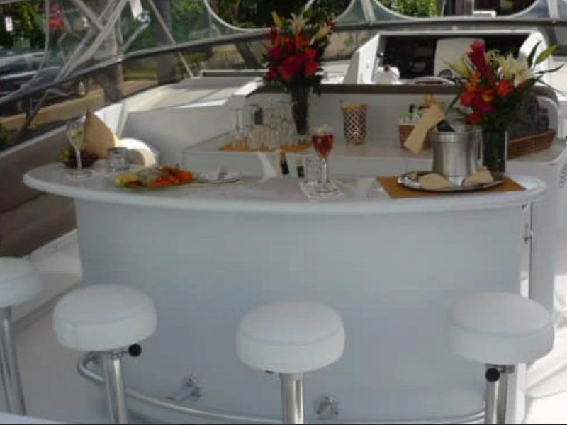 Entertaining flybridge lounge aboard the 100' Broward Yacht Charter in Fort Myers featuring a curved wet bar, bar stools, floral décor and comfortable outdoor seating.