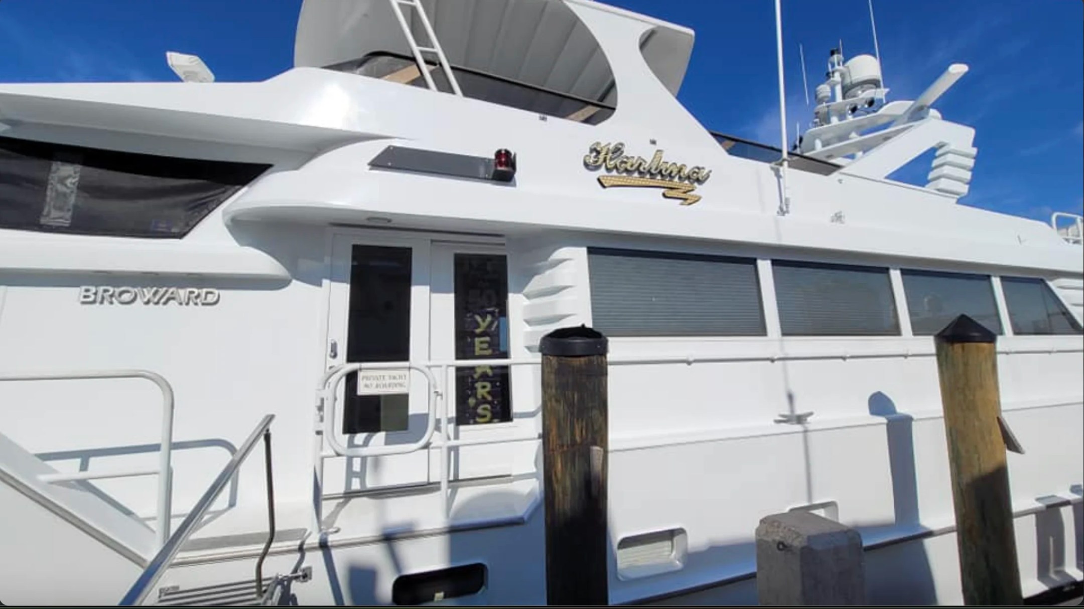 Portside view of the 100' Broward Yacht Charter docked at a Fort Myers marina showcasing the classic Broward profile, expansive side decks and elegant superstructure.
