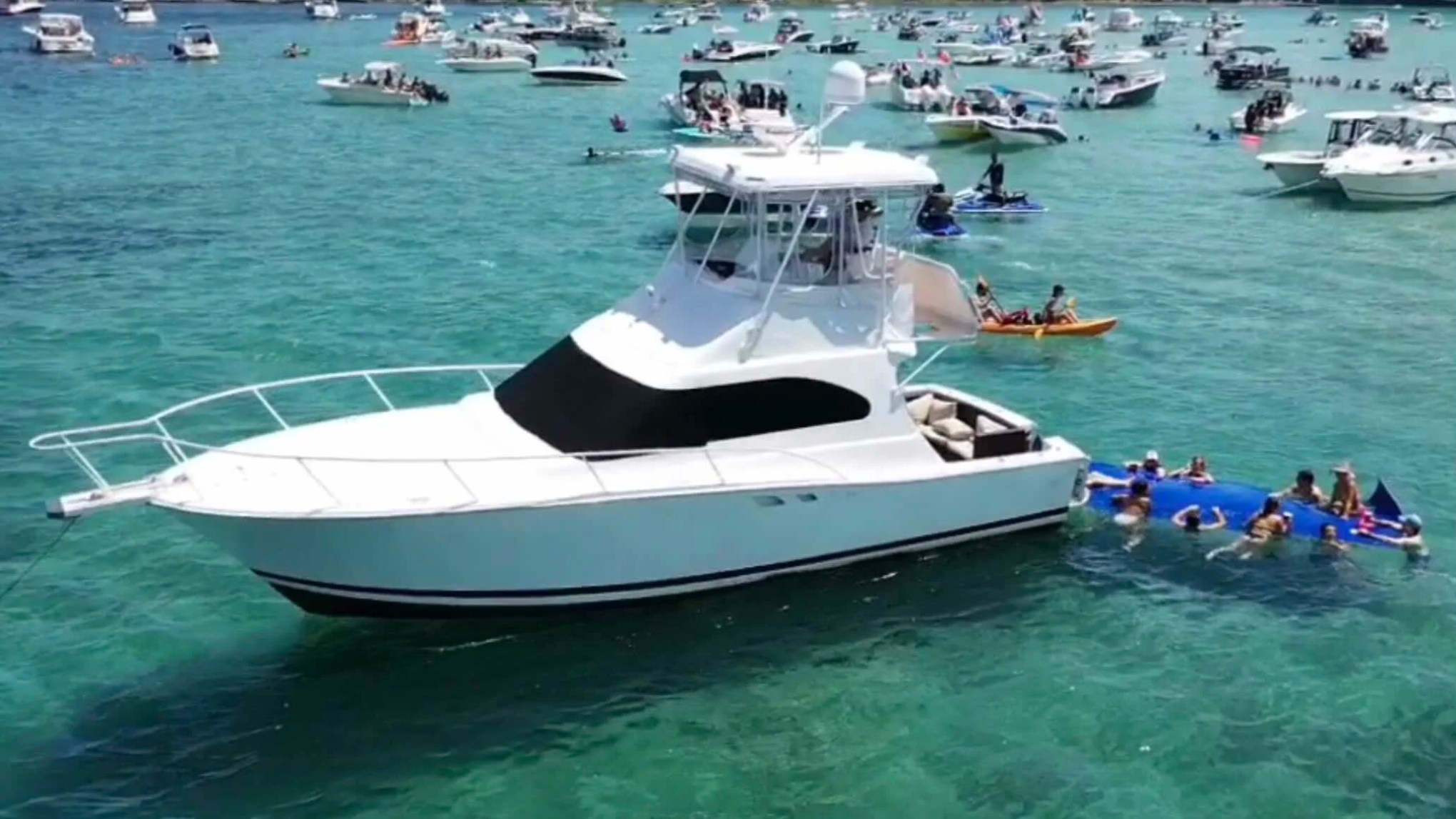 41' Luhrs Boat Rental anchored at the Hollywood sandbar with guests enjoying a floating mat in crystal-clear South Florida waters.