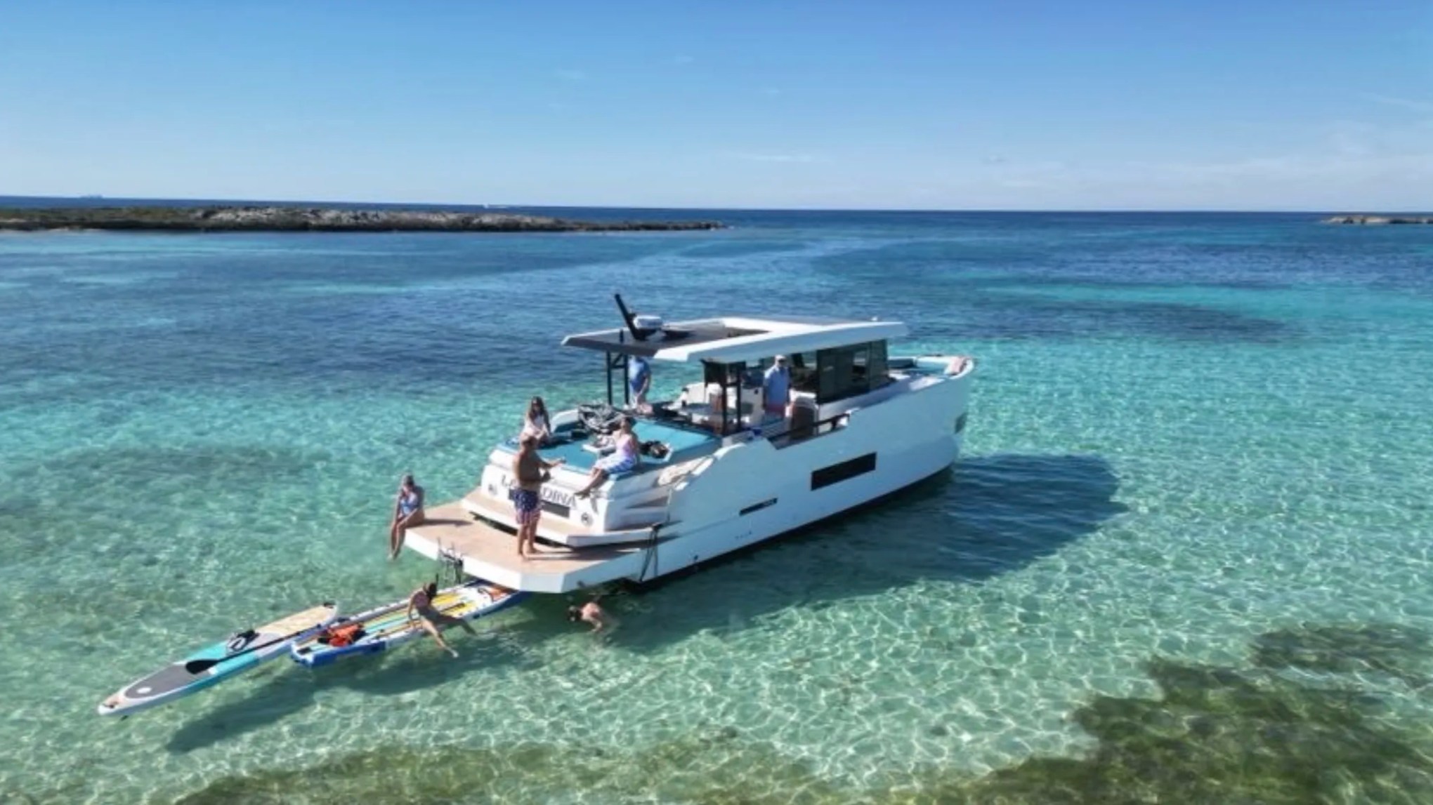 50' DeAntonio Yacht Charter anchored in the crystal-clear waters of Palm Beach with guests enjoying paddleboards and swimming beside the spacious aft swim platform.