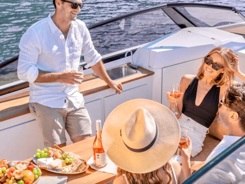 Friends enjoying food and refreshments around the social dining area aboard a 29' RAND Boat Rental in Riviera Beach, Florida.