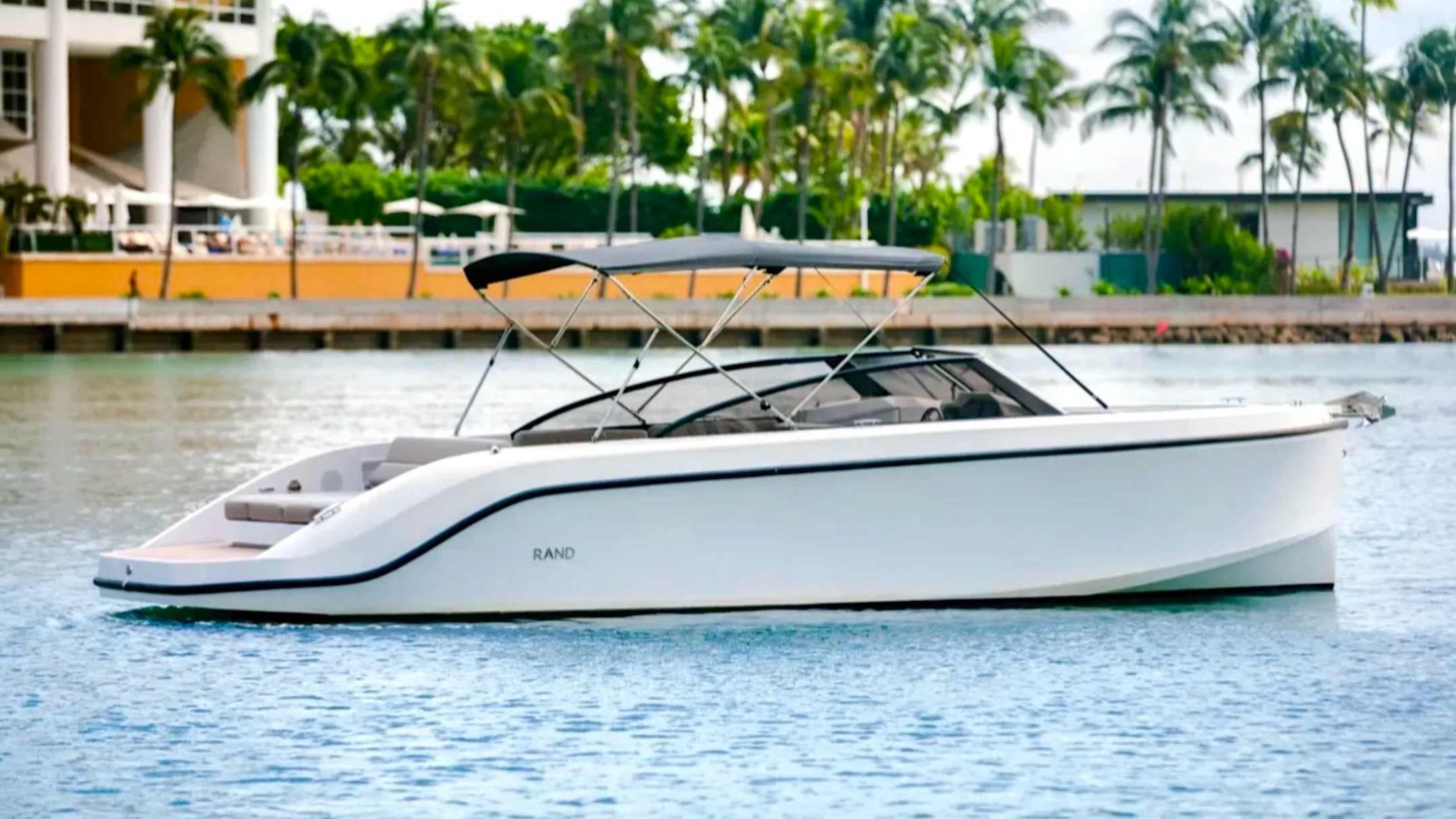 Side profile of a sleek 29' RAND Boat Rental with extended sunshade along the tropical waterfront in Riviera Beach, Florida.