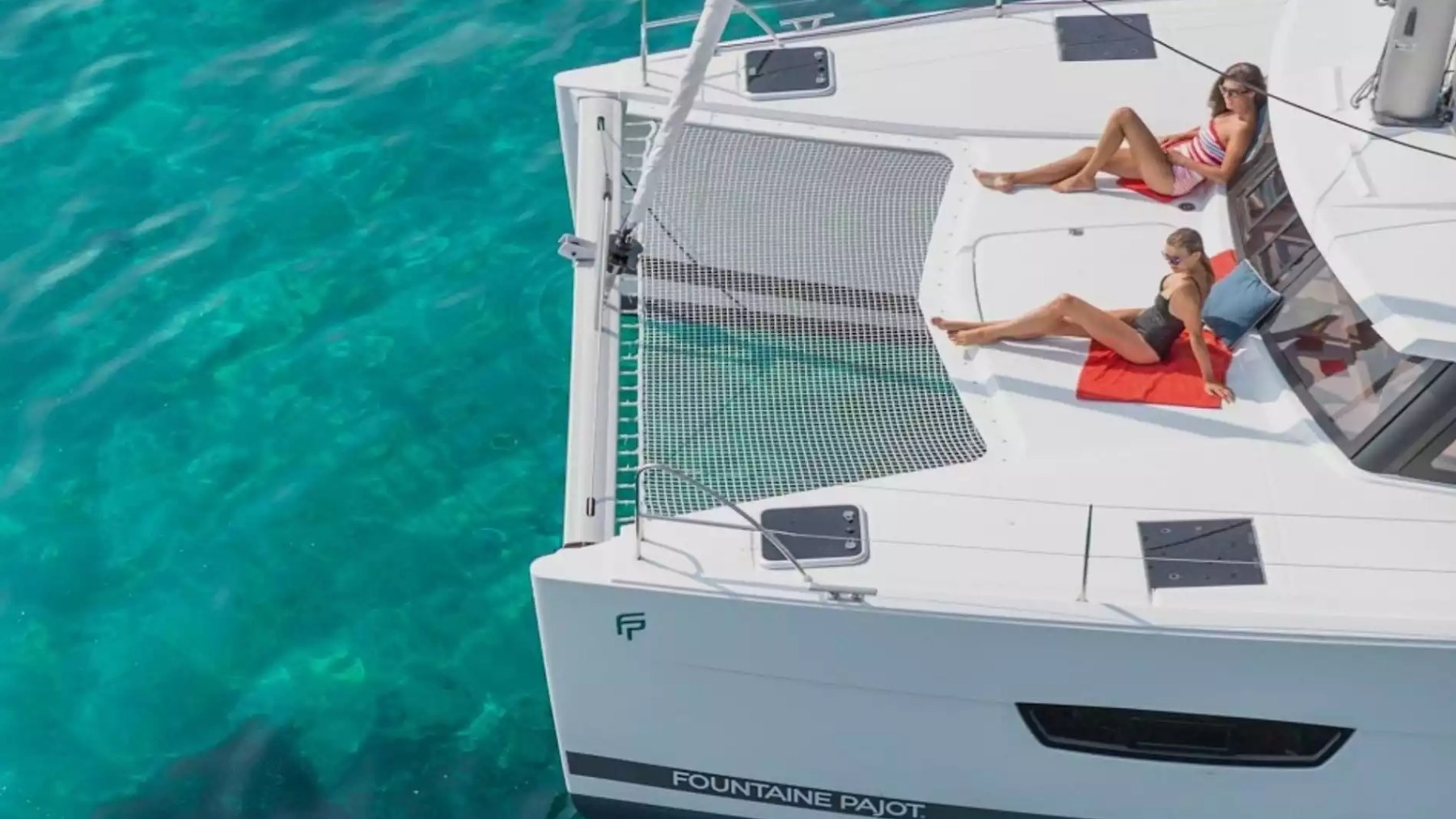Guests relaxing on the bow of a 40' Fountaine Pajot Boat Rental with catamaran trampoline over tropical waters.