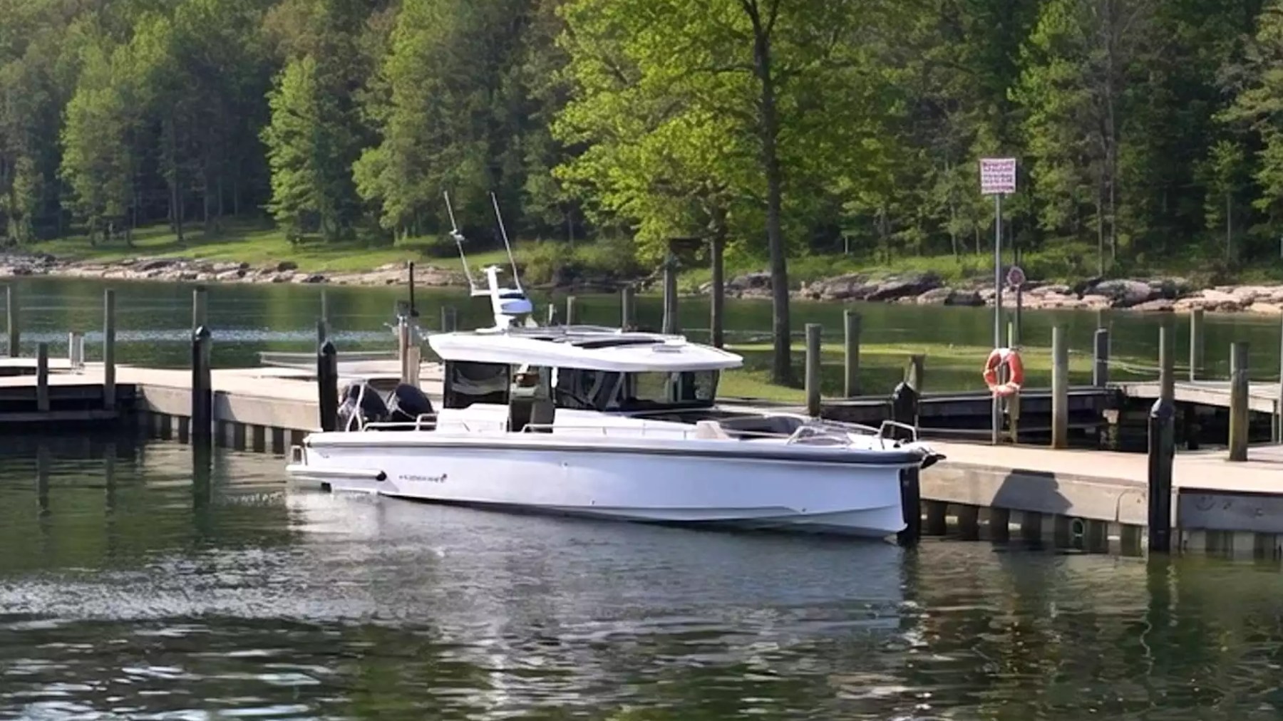 Axopar Boat Rental docked at a lakeside marina with wooded hills and calm water.