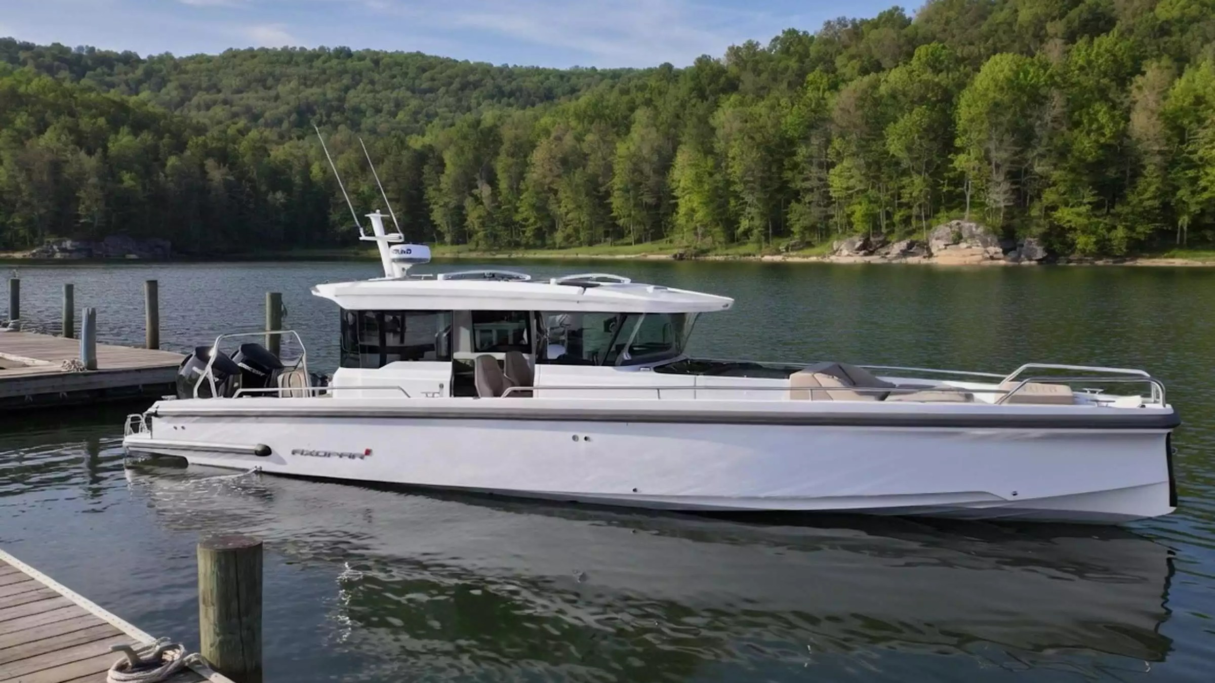 Axopar cabin boat with bow lounge seating docked beside a wooded lakeshore.