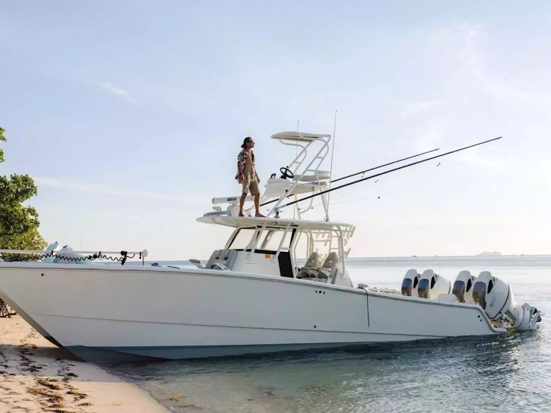 Center console boat with tower, fishing rods and multiple outboard engines positioned along a tropical shoreline.