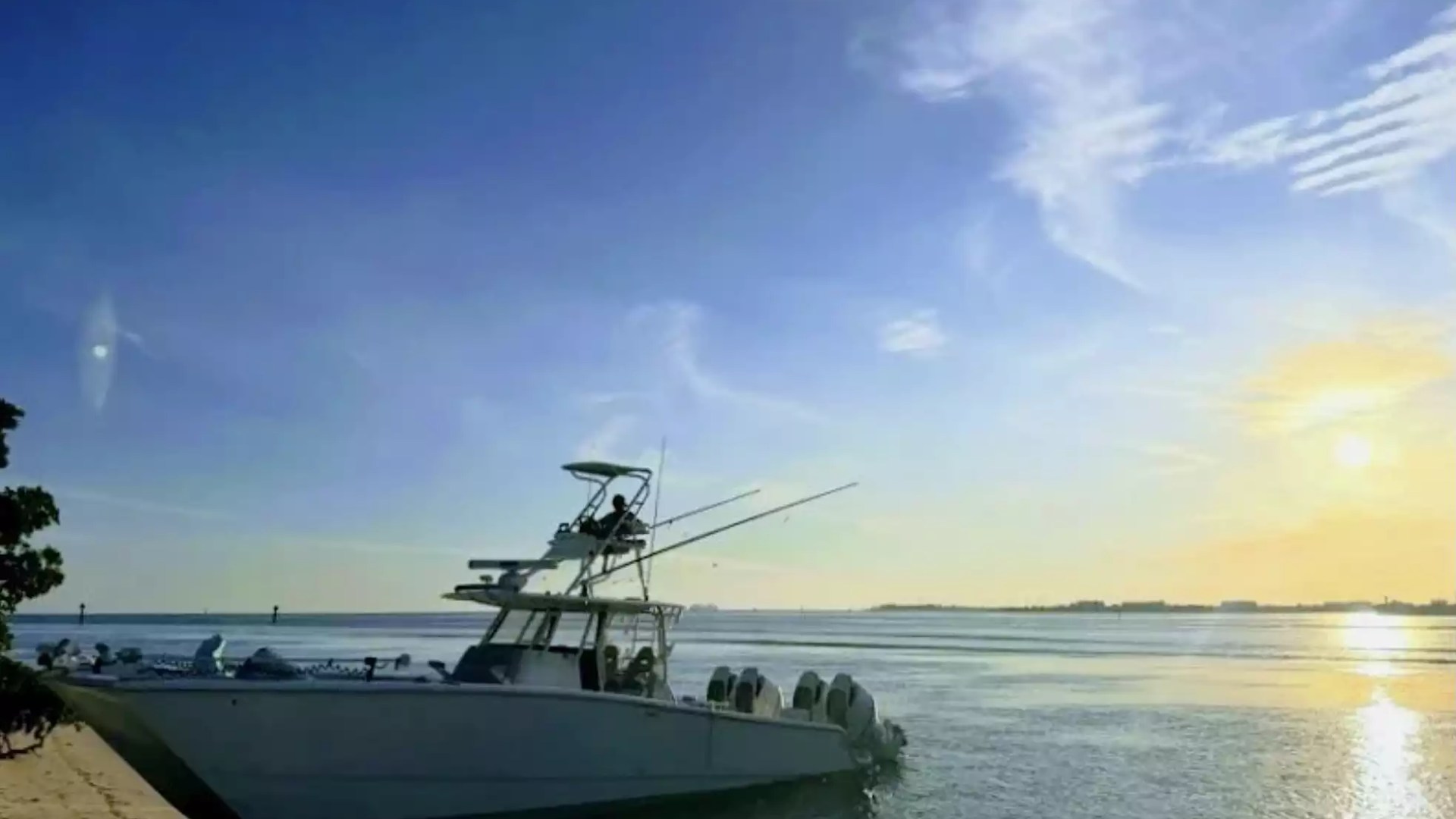 Center console fishing boat beached along a peaceful shoreline at sunset with tower, fishing rods and multiple outboard engines.