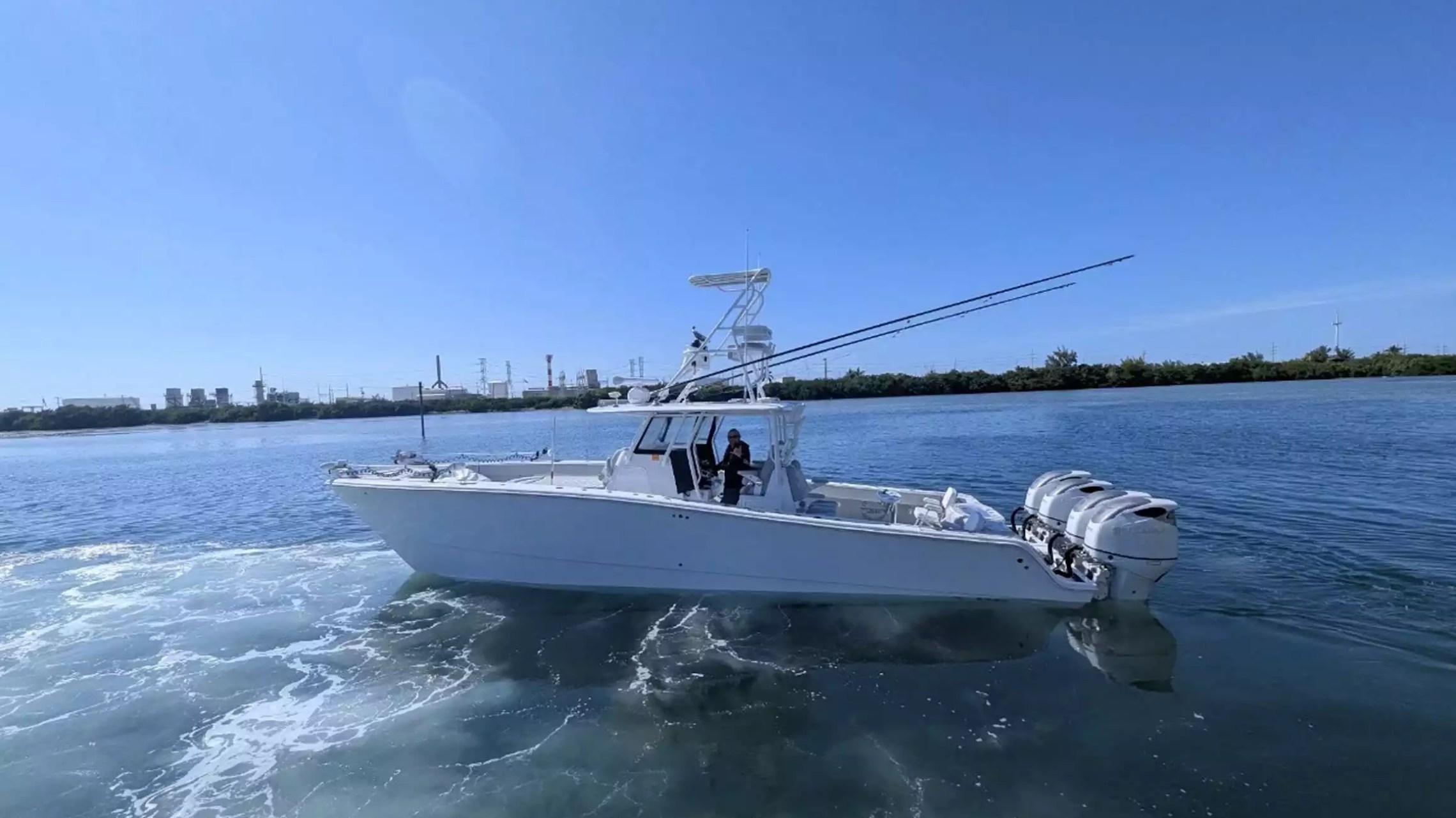 Center console fishing boat underway with tower helm, fishing rods and four outboard engines on open water.