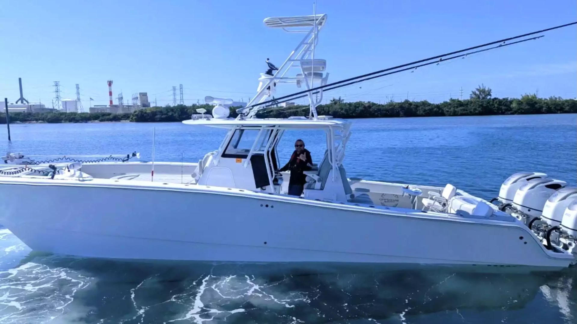 Center console fishing boat underway with elevated tower, fishing rods and multiple outboard engines.