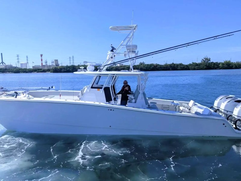 Center console fishing boat underway with elevated tower, fishing rods and multiple outboard engines.