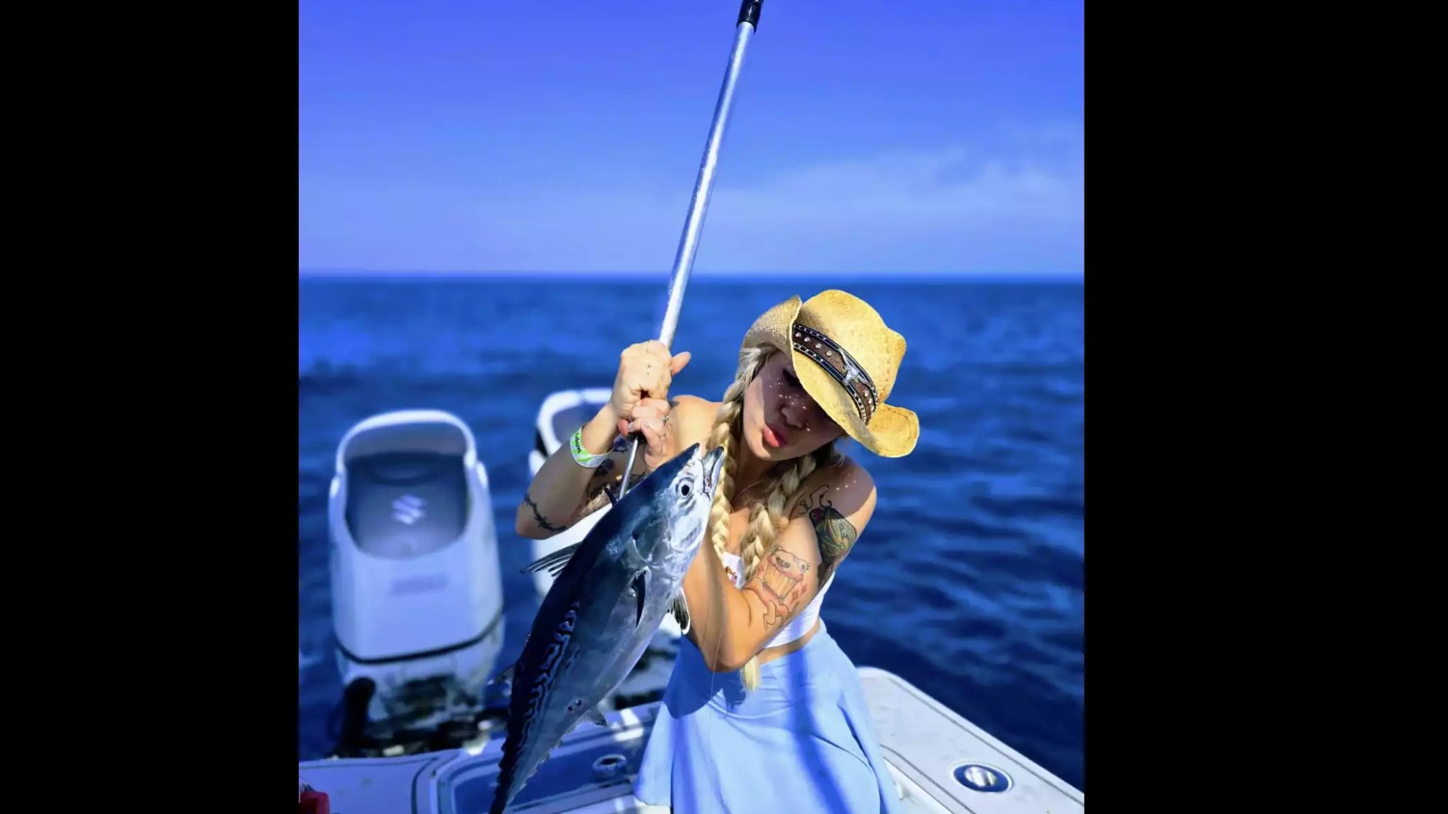 Woman holding a freshly caught tuna while sport fishing from a center console boat on open ocean waters.