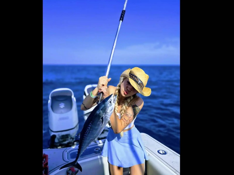 Woman holding a freshly caught tuna while sport fishing from a center console boat on open ocean waters.