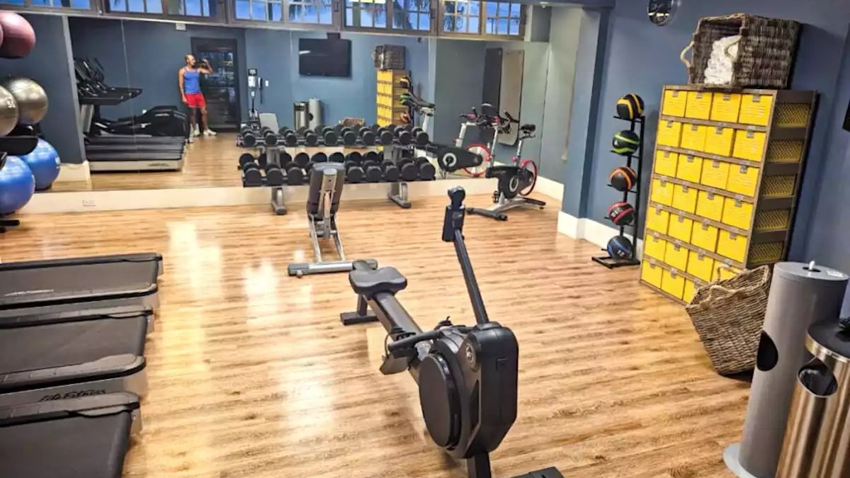 Fitness center with rowing machines, dumbbells, exercise bikes, treadmills and mirrored workout area.