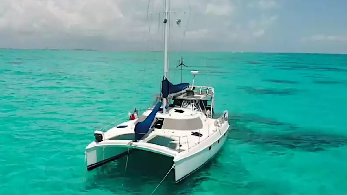 Sailing catamaran anchored in clear turquoise tropical water with twin hulls, tall mast and spacious deck.