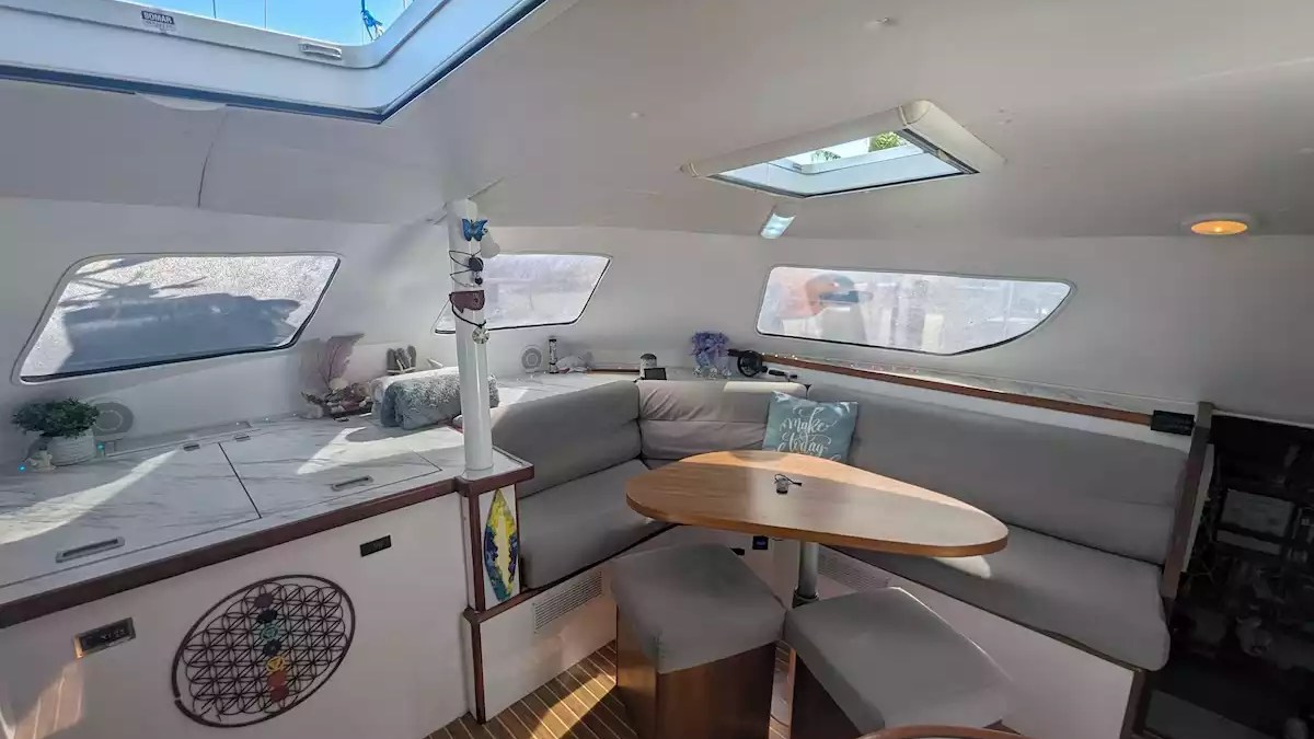 Sailing catamaran interior salon with wraparound seating, dining table, panoramic windows and overhead hatches.