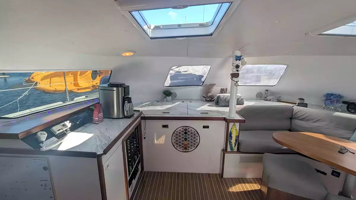 Sailing catamaran interior salon with wraparound seating, wood dining table, panoramic windows and large overhead skylight.