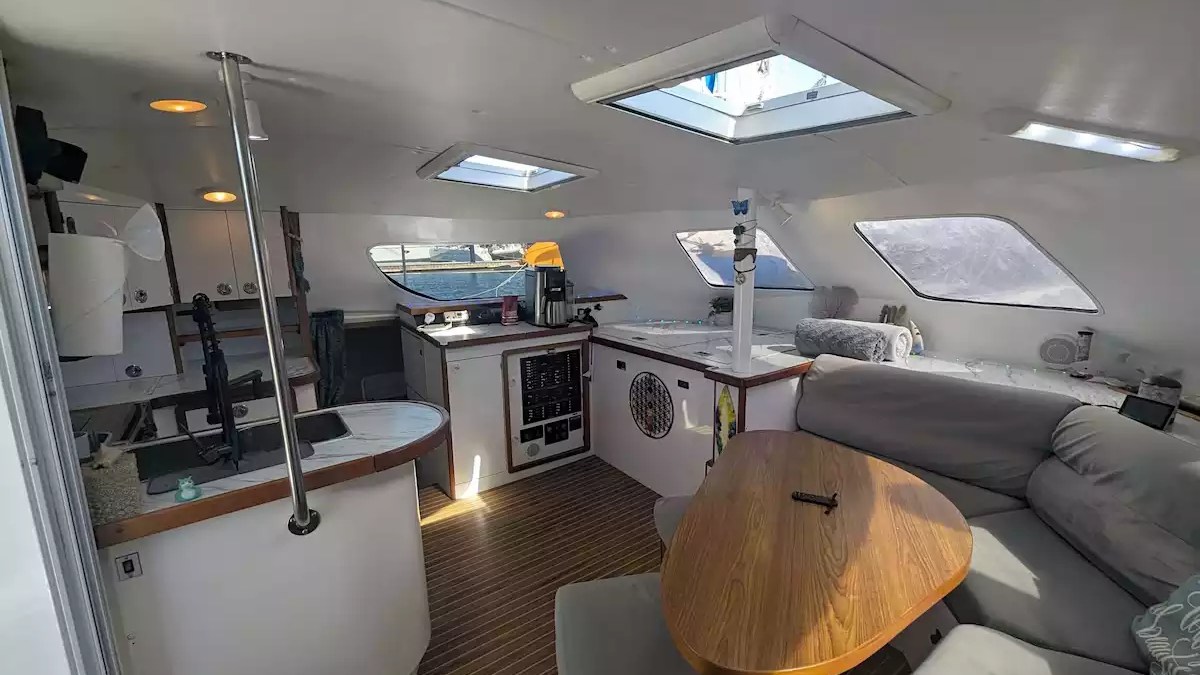 Sailing catamaran interior salon with dining table, wraparound lounge seating, skylights and galley area.