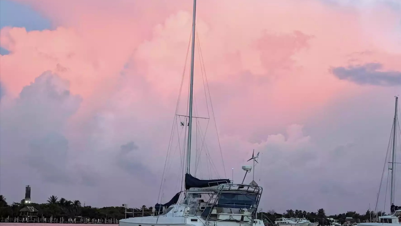 Sailing catamaran anchored at sunset beneath dramatic pink clouds and colorful evening skies.
