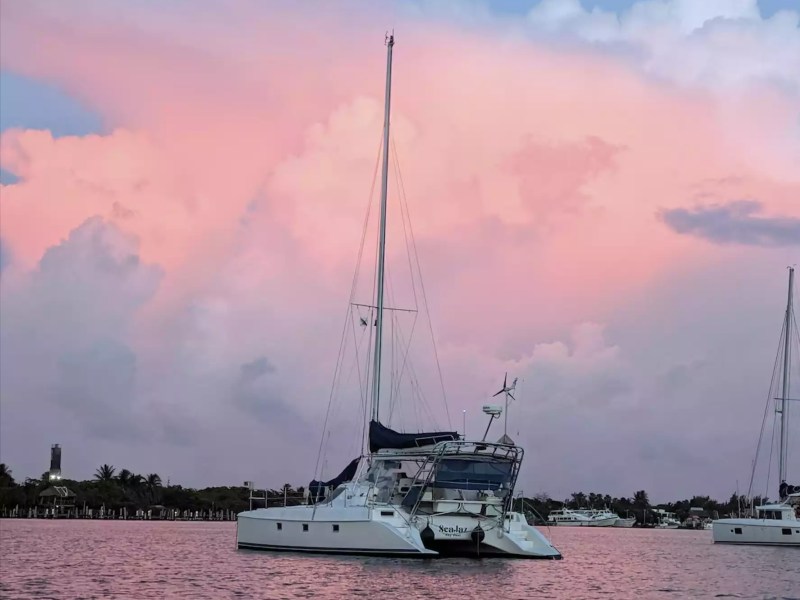 Sailing catamaran anchored at sunset beneath dramatic pink clouds and colorful evening skies.