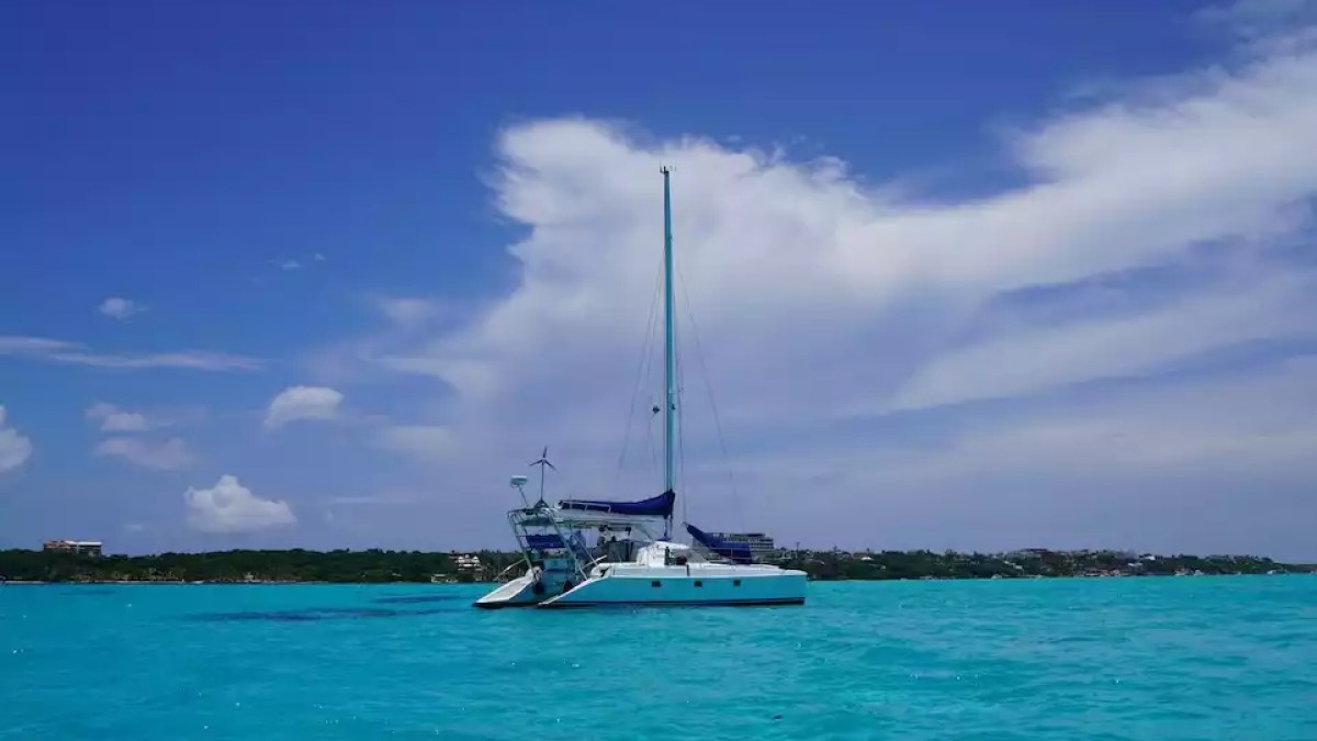 Sailing catamaran anchored in expansive turquoise water with tropical coastline and blue sky.