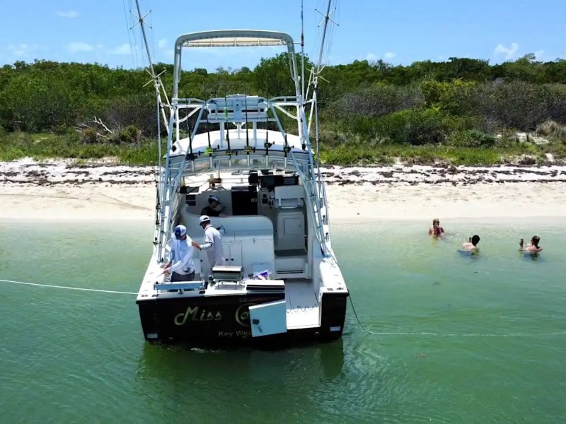 Sportfishing Boat Rental anchored near a secluded Key West beach with guests swimming in clear tropical water.